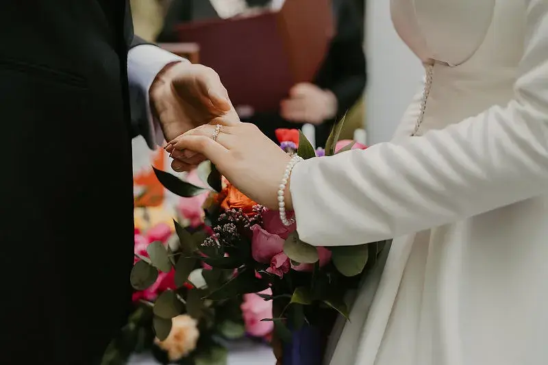 Zakładanie obrączki podczas ceremonii ślubnej przy bukiecie kwiatów Zakładanie obrączki podczas ceremonii ślubnej przy bukiecie kwiatów