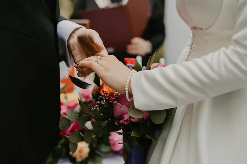 Zakładanie obrączki podczas ceremonii ślubnej przy bukiecie kwiatów Zakładanie obrączki podczas ceremonii ślubnej przy bukiecie kwiatów